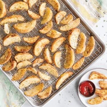 Nordic Ware sheet pan and cooling rack combination, shown filled with potato wedges on a colorful tile and terrazzo countertop