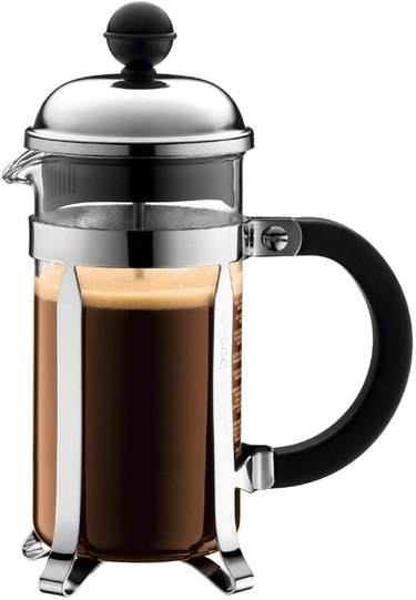 A Bodum Chambord French Press made of glass and stainless steel with metal feet and a round knob at the top.