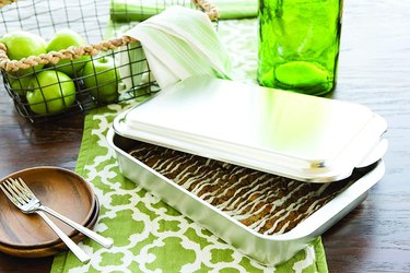 Nordic Ware 9X13 pan with lid, shown on a tabletop with the lid ajar, baked goods visible in the pan, and wooden dessert plates with forks