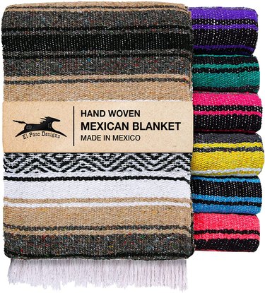 A stack of 7 Mexican blankets in various colors next to a folded brown and tan-colored blanket facing forward. The label says hand woven Mexican blanket, made in Mexico.