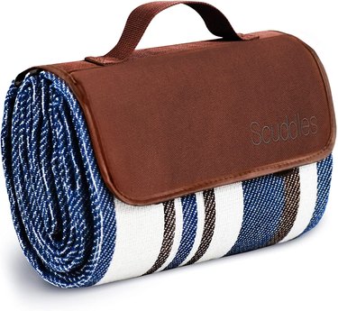 Navy blue, white, and brown striped blanket folded up into a tote with a brown handle and partial cover.