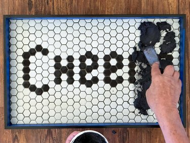 Tile grout spread into cracks between black and white tiles reading "Cheers"