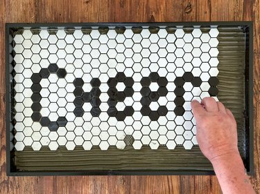 Black and white tiles reading "Cheers" set atop green spread mortar on board