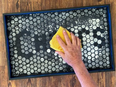 Yellow sponge being used to clean black grout off black and white tiles