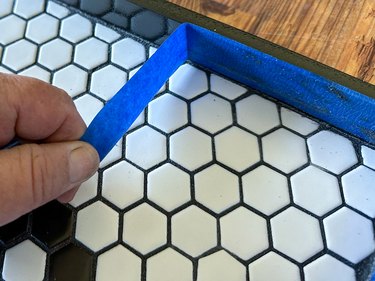 Blue painter's tape being pulled off side of black and white tile tray
