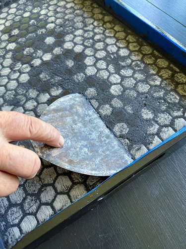 Metal scraper removing black grout from black and white tiles