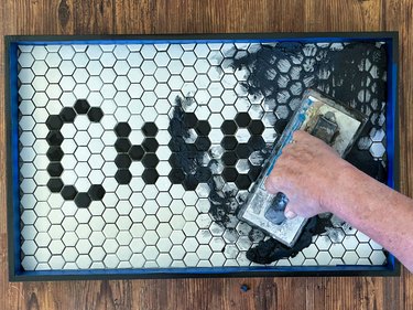 Tile grout pushed into cracks between black and white tiles reading "Cheers"