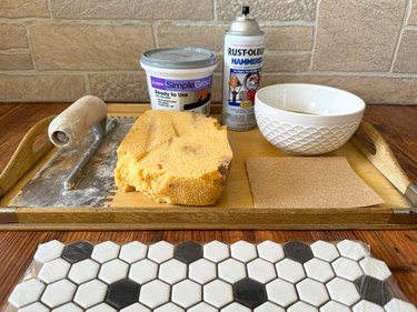 Black and white tiles set next to a sponge, spray bottle, white bowl and grout in a tub