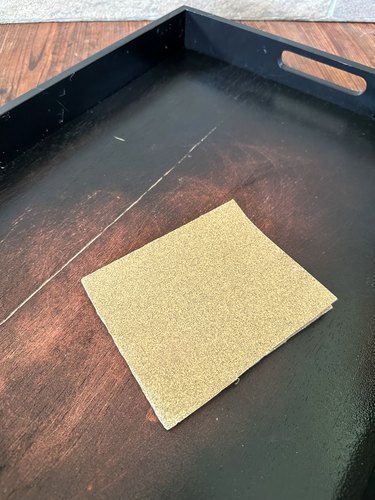 Square section of light brown sandpaper set atop wood tray