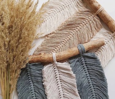 Two Macrame Feather Kits with neutral colors like off-white, blue, and tan. The sticks the feathers hang off of are pieces of driftwood.