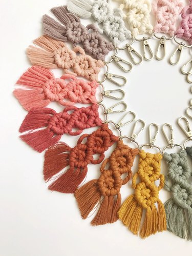 A circle of macrame keychains in a rainbow of colors. The macrame part of the keychain makes a shape similar to the number 8 and there's fringe at the bottom. The clips are like mini carabiners.