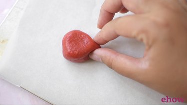 Shaping strawberry cookies on lined baking sheet.