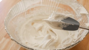 Stiff peaks of whipped cream on mixer attachment.
