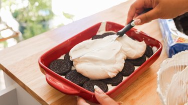 Using an offset spatula to spread whipped cream over Oreos in a baking dish.