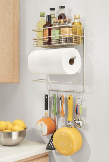 Paper towel holder with storage above it for oils and spices and hooks below it for cooking tools.