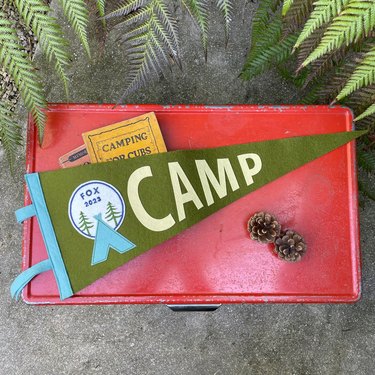 Green felt pennant reading "CAMP" on top of a red suitcase
