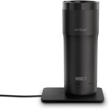 Large black travel mug on a warming pad with an icon to show how much battery life the mug has.