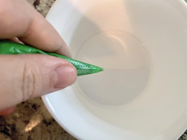Green royal icing in piping bag held in hand over small white bowl