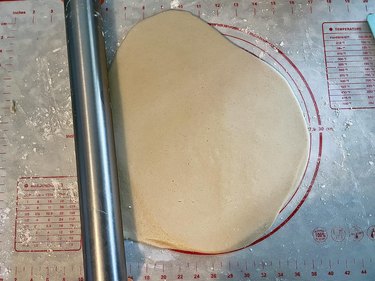 Flat dough circle and silver rolling pin against silicone mat background