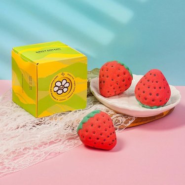 Three strawberry-shaped bath bombs with yellow box