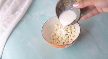 Pouring heavy cream into bowl with white chocolate chips.