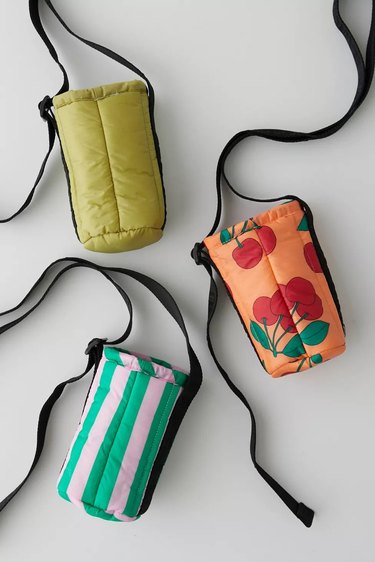 Three puffy BAGGU water bottle holders shot from above. One is chartreuse, one is green and pink vertical striped, and another is peachy orange with a cherry print on it. All have adjustable black straps.