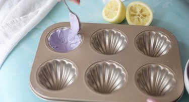 Spooning purple white chocolate into madeleine pan.