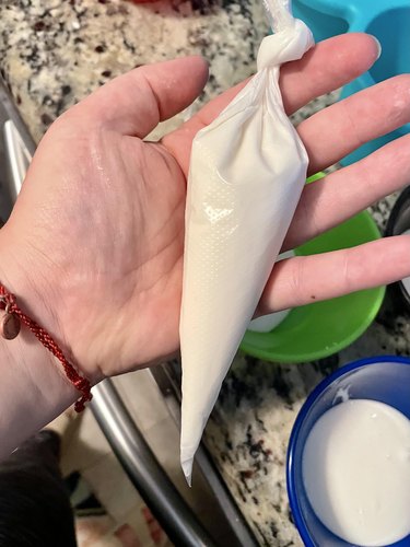 Hand holding piping bag full of white royal icing