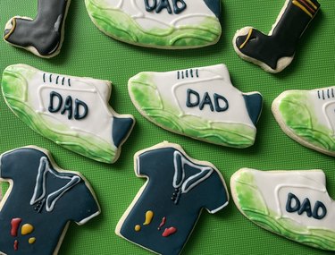 Completed cookies shaped like grass-stained sneakers, condiment-stained dark blue polo shirts and black socks with holes in the heels on a bright green background