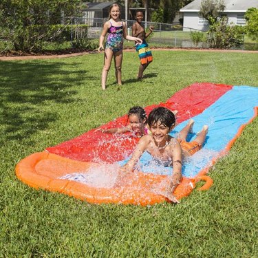 Two kids using the H2OGO! Double Lane Water Slide in a grassy backyard.