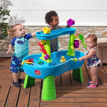 Three toddlers playing with Step2 Splash Water Table on a patio.