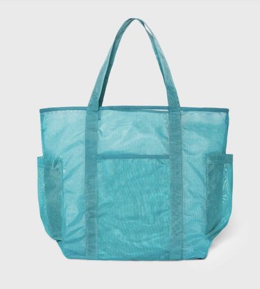 Mesh beach bag in 'green' (looks more turquoise) with two large side pockets. Pictured against an off-white background.