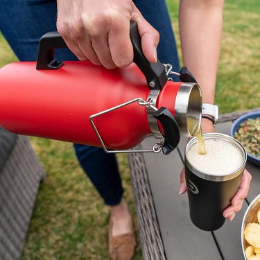DrinkTanks 32 ounce growler, pictured outdoors pouring into the accompanying insulated tumbler