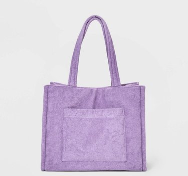 Lilac colored beach bag in a terry cloth-like fabric with a large front pocket and matching handles. It's pictured against an off-white background.