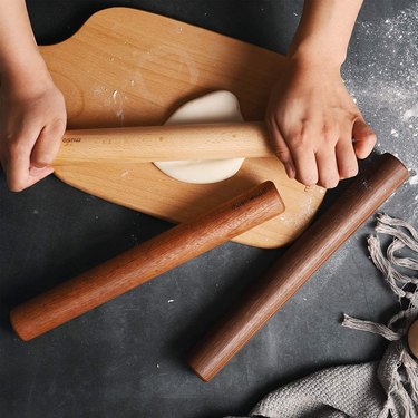 Compact rolling pins from Muso Wood, pictured in beech, walnut and sapele versions, with hands rolling a small round of dough on a cutting board