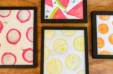 Prints of watercolor dragon fruits, watermelon slices, lemon slices and mandarin oranges in black frames