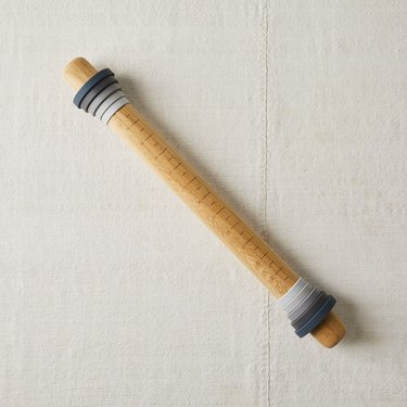 Food 52 adjustable rolling pin, depicted with its spacing rings in place, against a background of coarse white linen