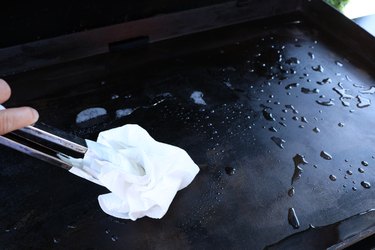 cleaning flat top grill with tongs and paper towels