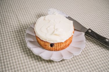 A topless blueberry muffin topped with a layer of vanilla frosting