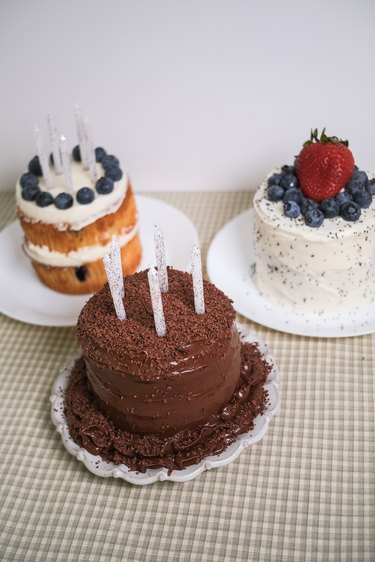 Three mini cakes, including a chocolate cake with chocolate frosting, a blueberry cake with vanilla frosting and a poppy seed cake with lemon frosting