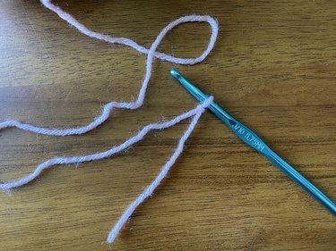 Pink yarn tied on a slip knot around a blue crochet hook.