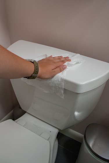 wiping down the toilet with a disinfectant wipe