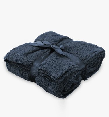 Barefoot Dreams CozyChic Throw Blanket in color indigo. It's folded in a square shape and wrapped up in a matching bow.
