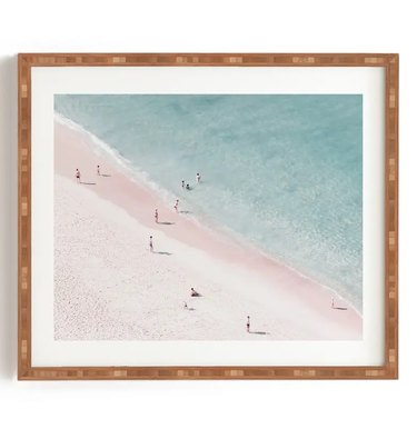 Abstract beach print. The ocean is a light blue and the sand is an ombre pastel pink. It's similar to a drone shot because the people on the beach all look very small and the POV is from above.