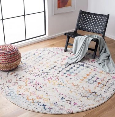 Colorful, circular geometric-print area rug. It's mostly white with a pink, blue, yellow, orange, and purple design.