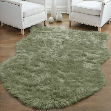 Green sheepskin rug situated in front of two white lounge chairs.