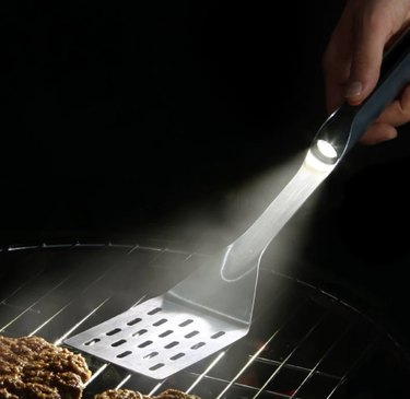 A nighttime image of a spatula with a built-in light getting ready to flip two easily-seen burgers .