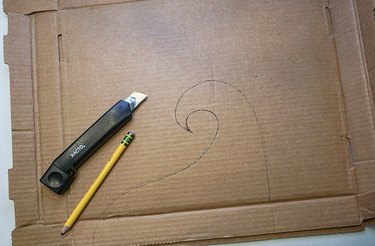 An X-Acto knife and pencil sitting atop a piece of cardboard, ready for cutting