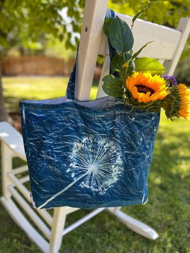 Solar print tote bag filled with flowers hanging on a white rocking chair in the backyard