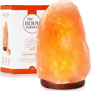Pink Himalayan salt lamp next to its box. The lamp has a round wooden base and a dimmer switch.